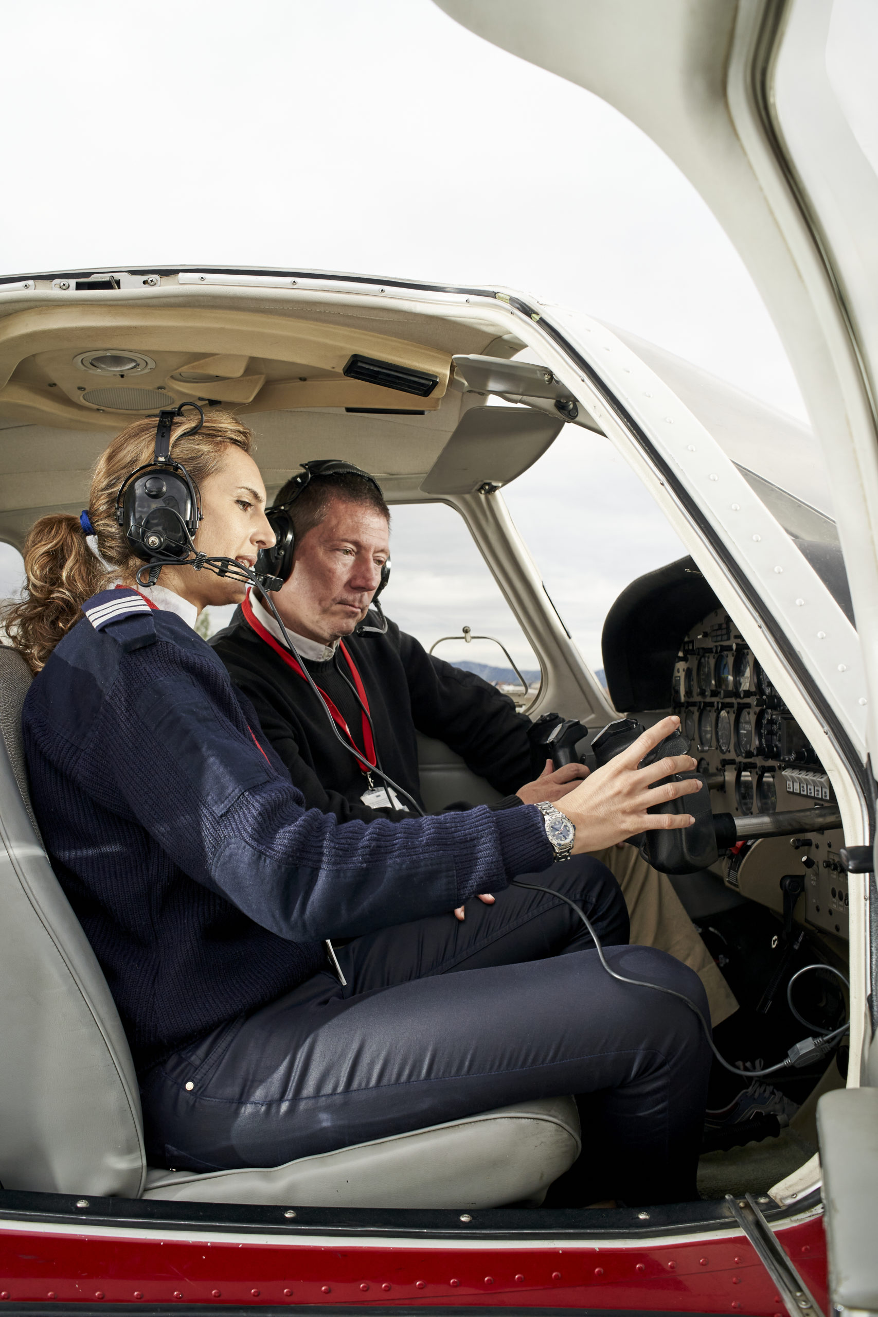 Pilot in training and flight instructor in the cockpit of an airplane. Portrait of attractive young pilot with headphones preparing to fly. He is sitting next to the female instructor and looking at the board.